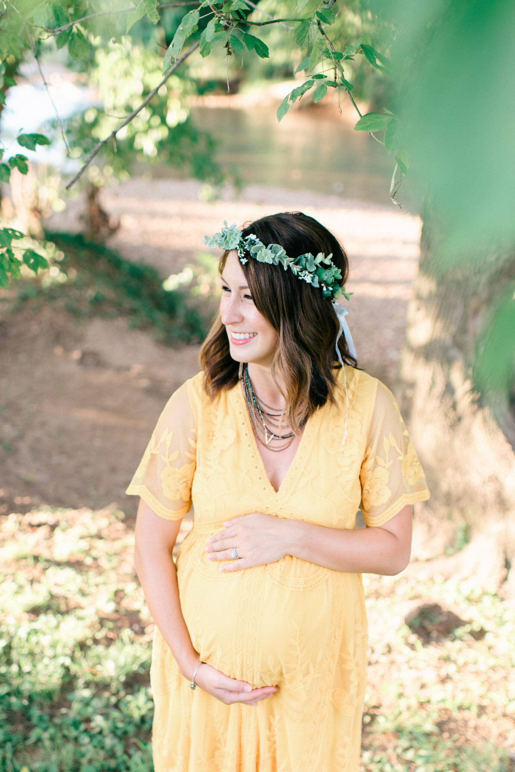 Bentonville Maternity Photographer Captures pregnant woman standing near a creek at sunset, with warm light illuminating her baby bump.