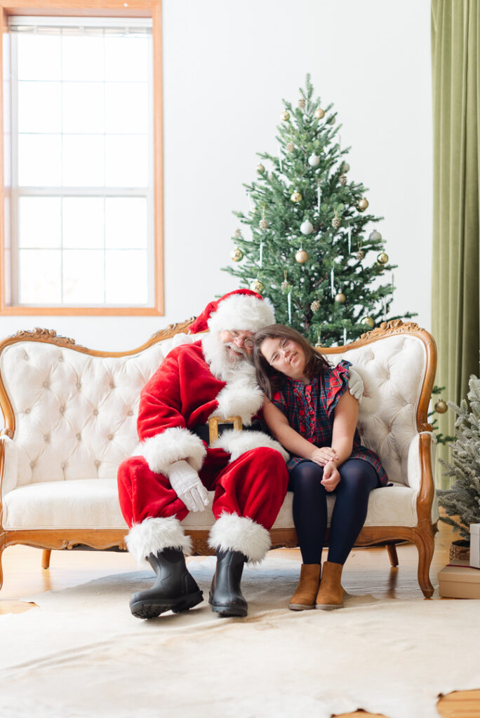 A little girl sitting next to Santa and smiling for a picture. 