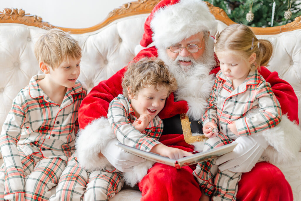Three kids in pajamas reading a book with Santa.