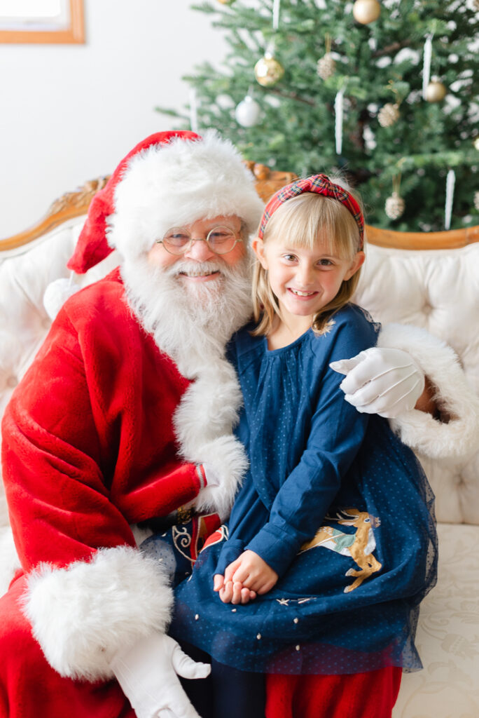A little girl sitting on Santa's lap and smiling for a picture. 
