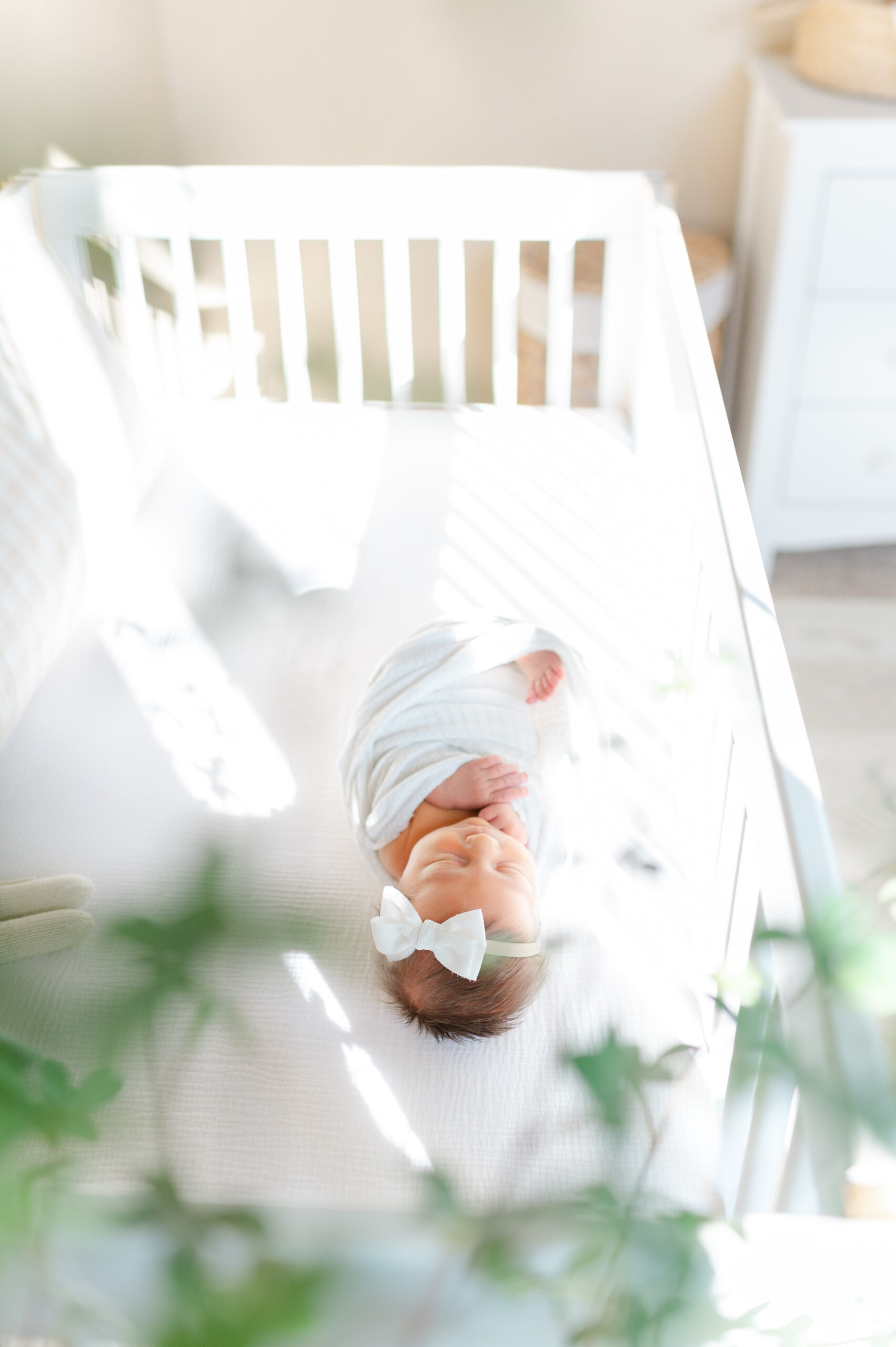 Newborn baby swaddled in a blanket, lying in a crib in a softly lit nursery during an in-home newborn photography session in Bentonville.