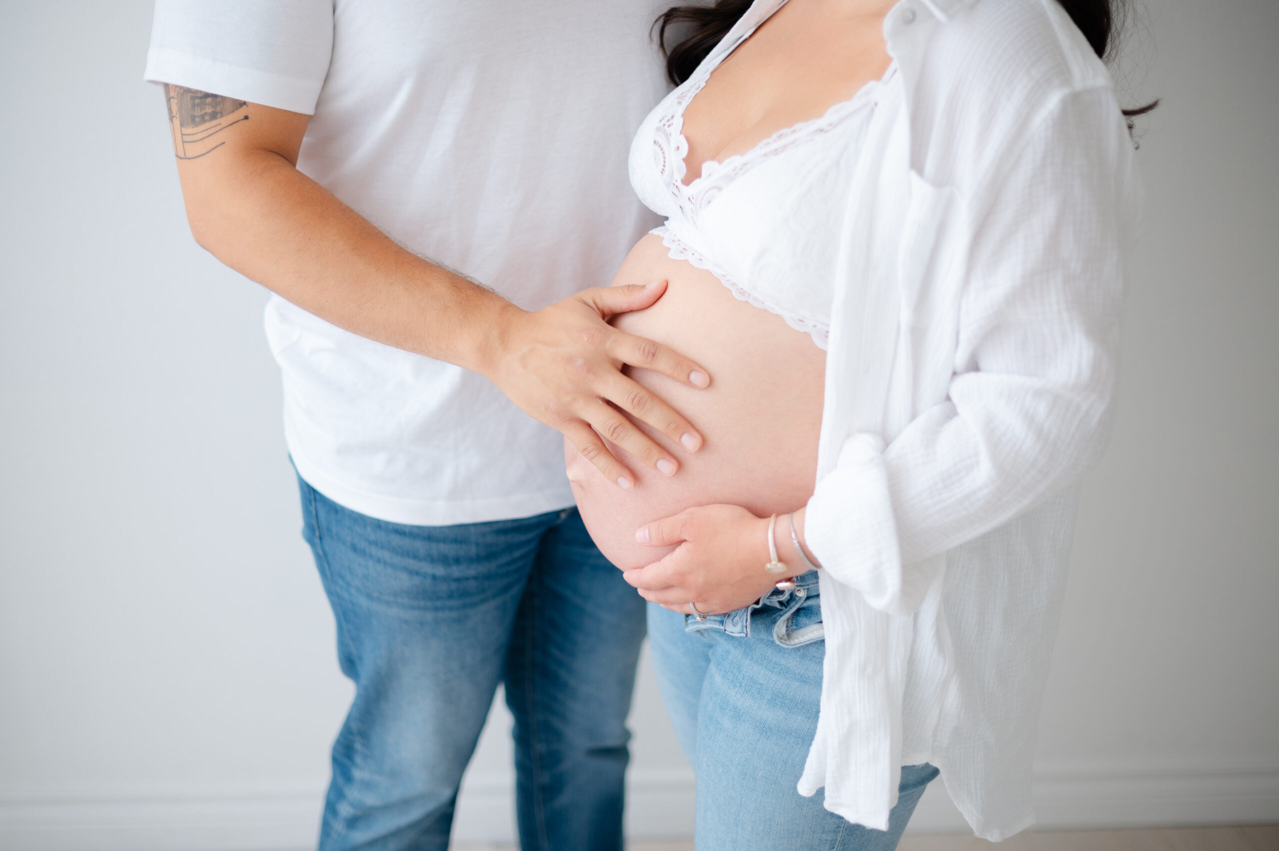 Close-up of NWA pregnant couple with hands lovingly placed on the mother’s bare baby bump.