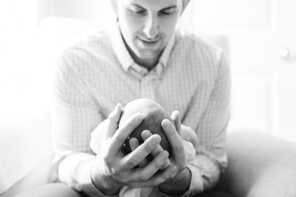 A black and white newborn portrait by NWA photographer with a father holding a newborn baby in his hands.