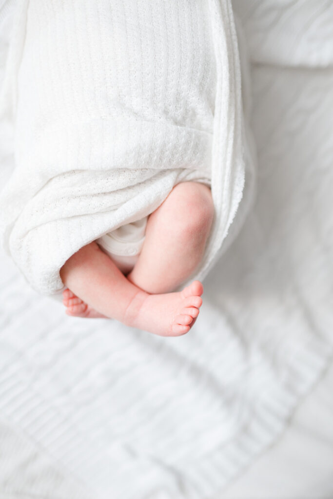 A close-up of tiny newborn baby toes peeking out of a swaddle, atop a soft, neutral-toned blanket. Captured by one of the talented NWA newborn photographers, this image beautifully preserves the details of newborn phase.