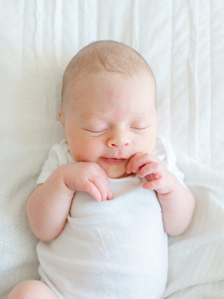 Newborn baby asleep on a cozy white blanket with soft natural light from a window — example of natural lighting for at-home newborn photography.