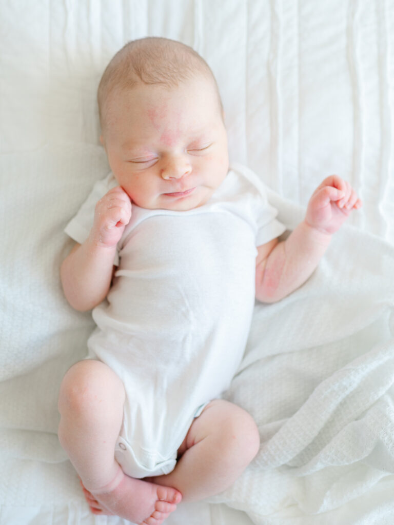 Newborn baby asleep on a cozy white blanket with soft natural light from a window — example of natural lighting for at-home newborn photography.