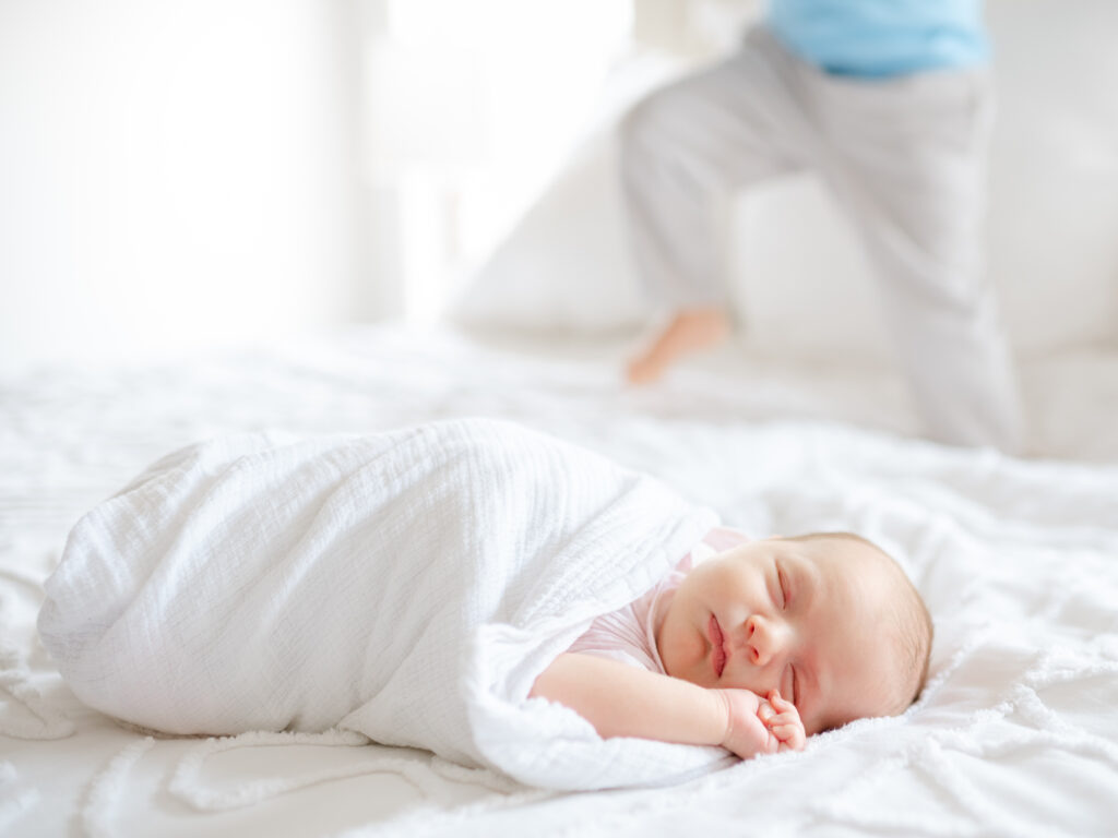 Newborn baby asleep on a cozy bed with soft natural light from a window — example of natural lighting for at-home newborn photography.