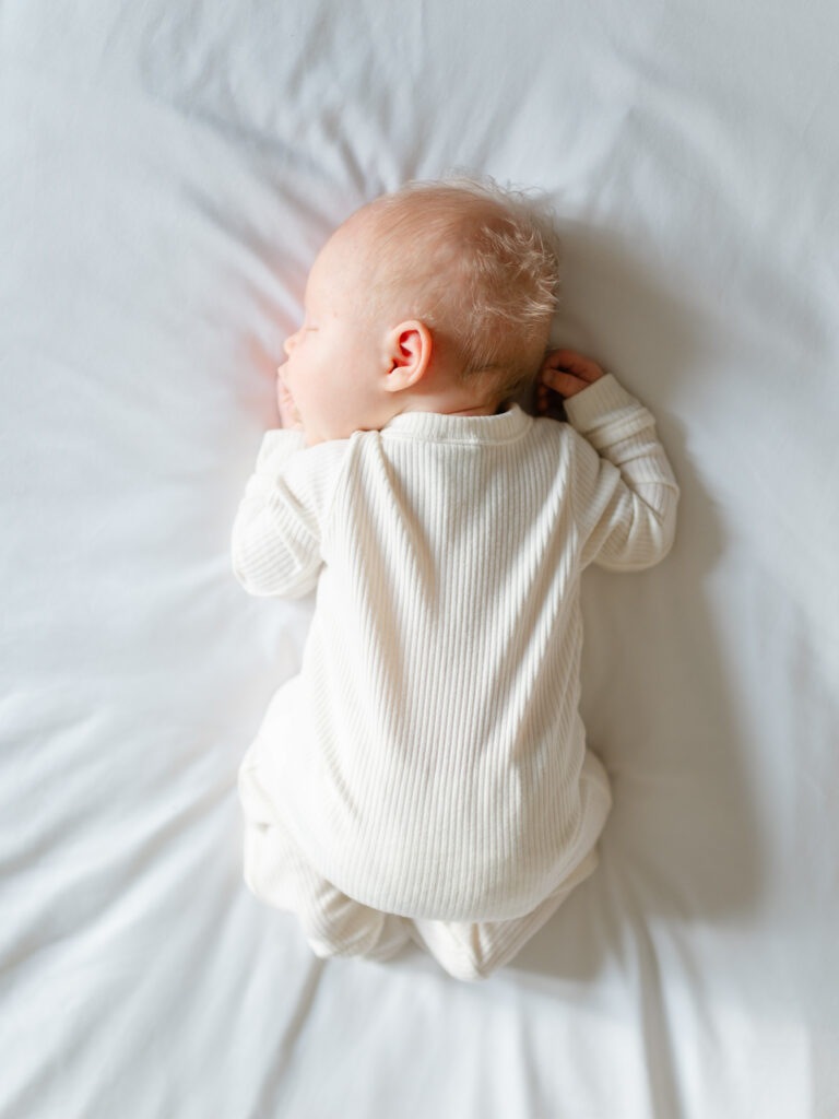 Newborn lying on soft bed with neutral linens and a clean background for a minimal, timeless look.