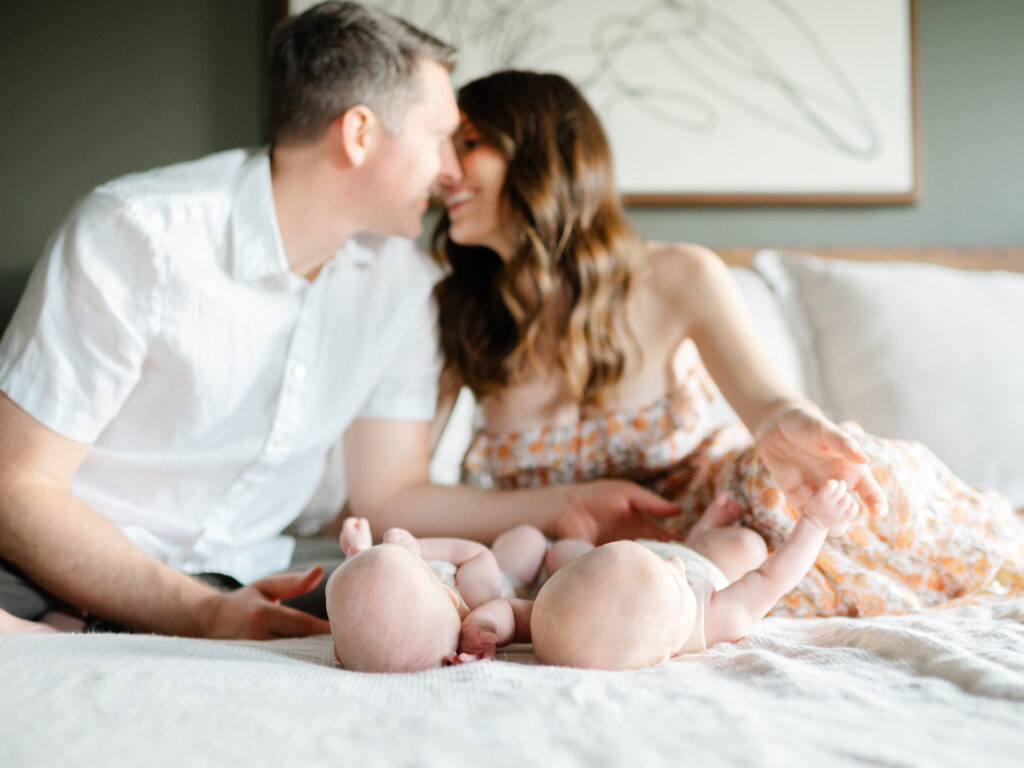 parents kissing and snuggling twin girls in bedroom during lifestyle newborn photography session