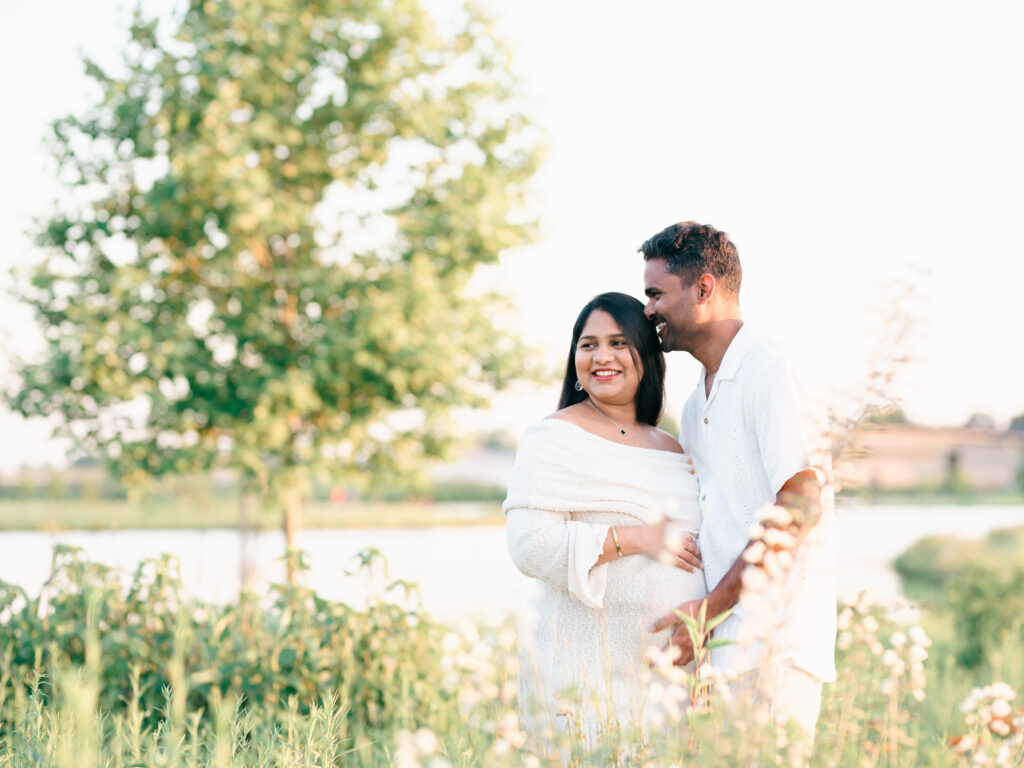 Pregnant woman smiling while her partner holds her belly in Bentonville, Arkansas