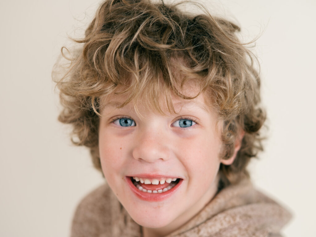 Close-up of a young child with curly hair laughing during school photo day, photographed by Northwest Arkansas Photographer Leslie Nice